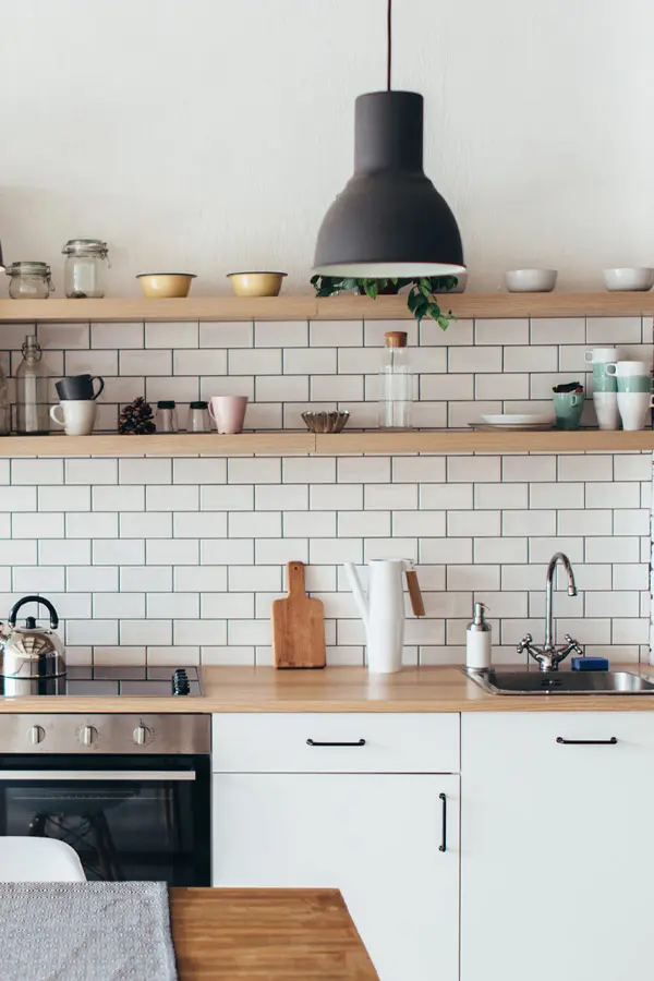 Cocina de tonos claros con muebles en madera y azulejos imitación ladrillo blanco.